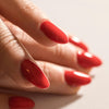 Image of a model's fingers with red acrylic and gel nails, nails are long, neutral background.