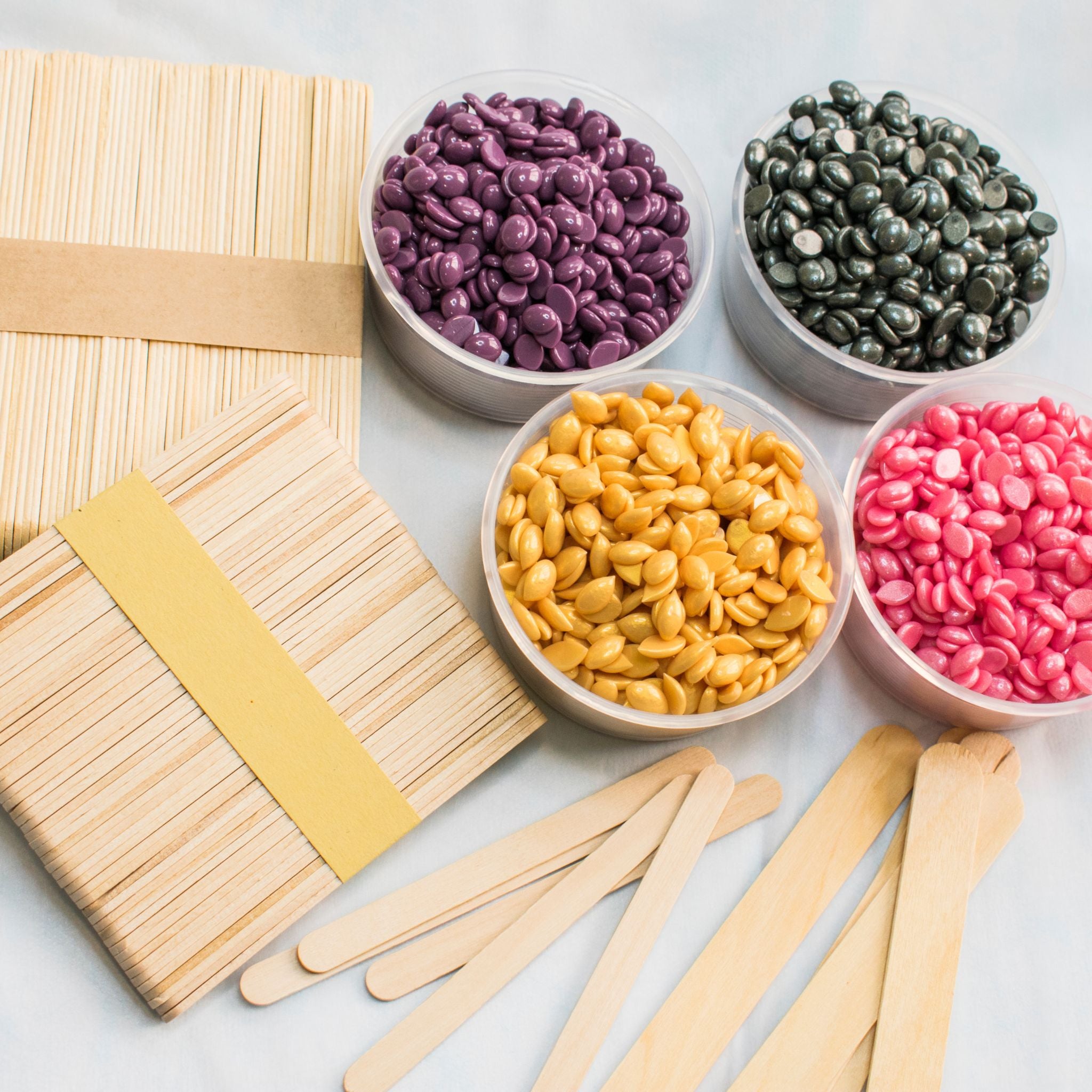 Bowls of colorful wax and wooden sticks on a light background