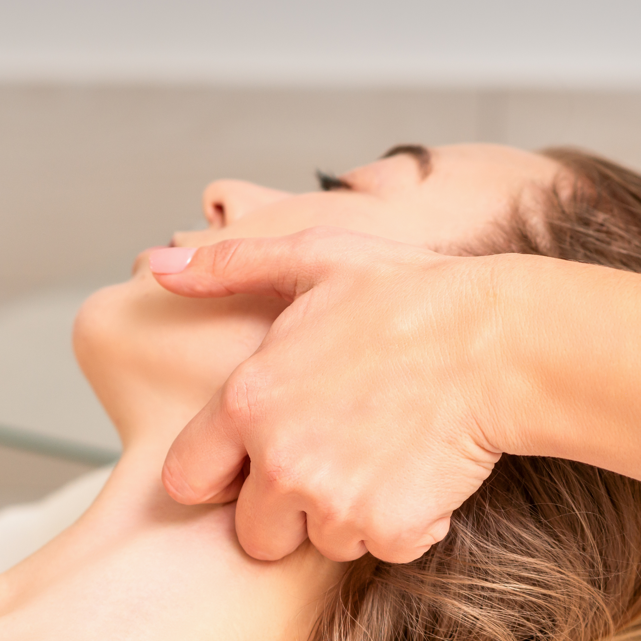 Close-up of a person receiving a facial and neck massage, with a therapist's hands pressing along the jawline and neck.