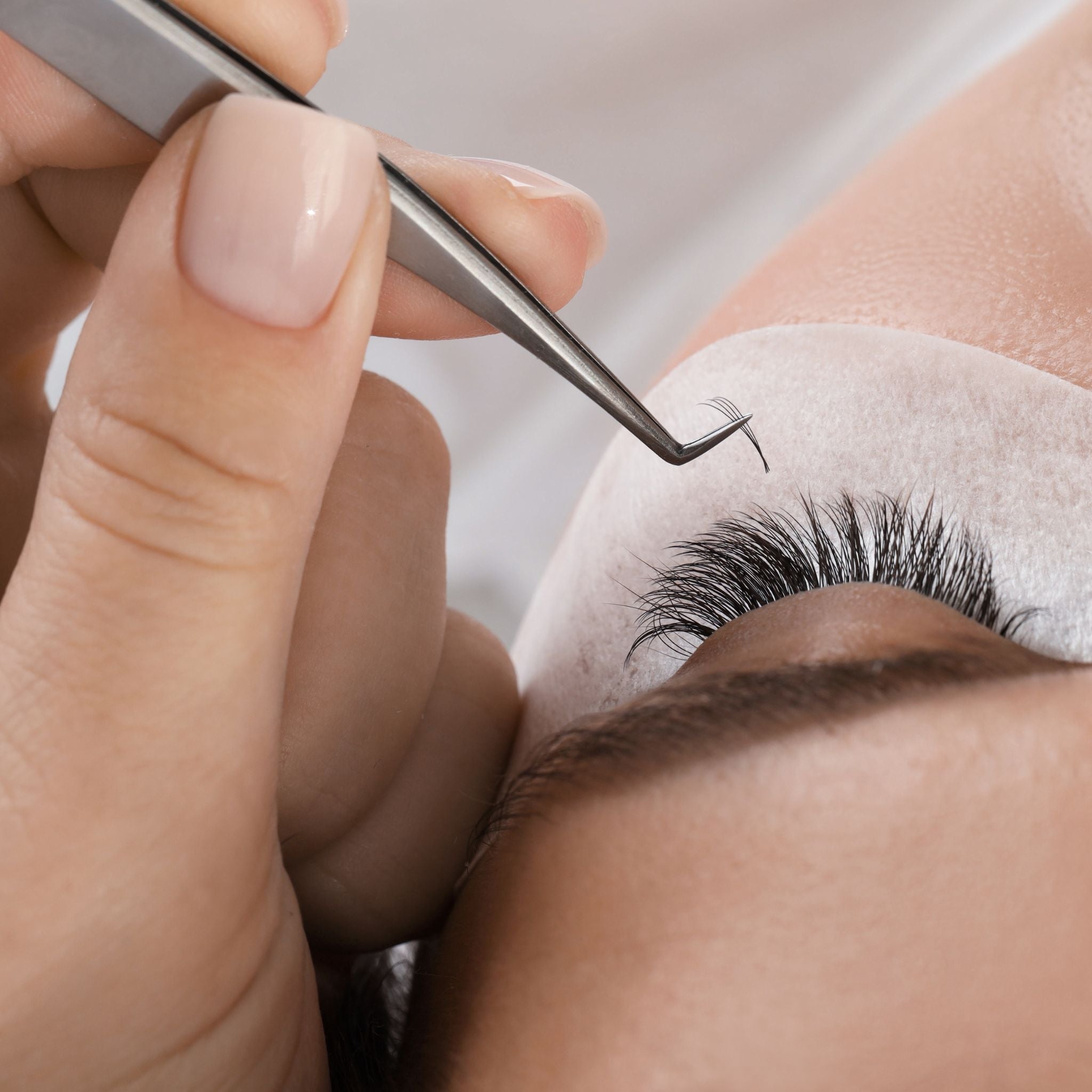 Eyelash extension process with tweezers and adhesive on a neutral background