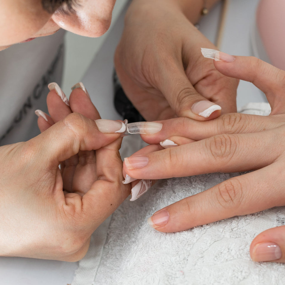 Person getting false nails applied with a focus on hands.