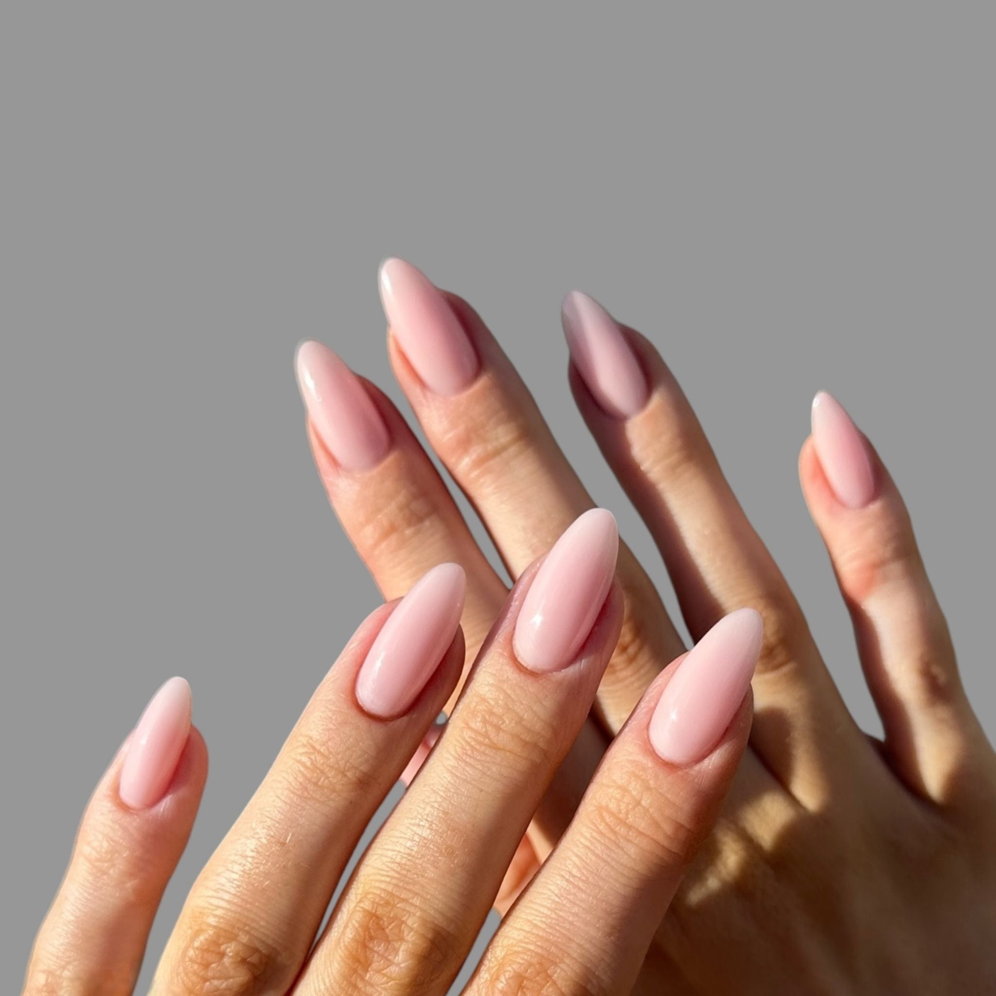 Hands with long pink gel nail polish on a light grey background