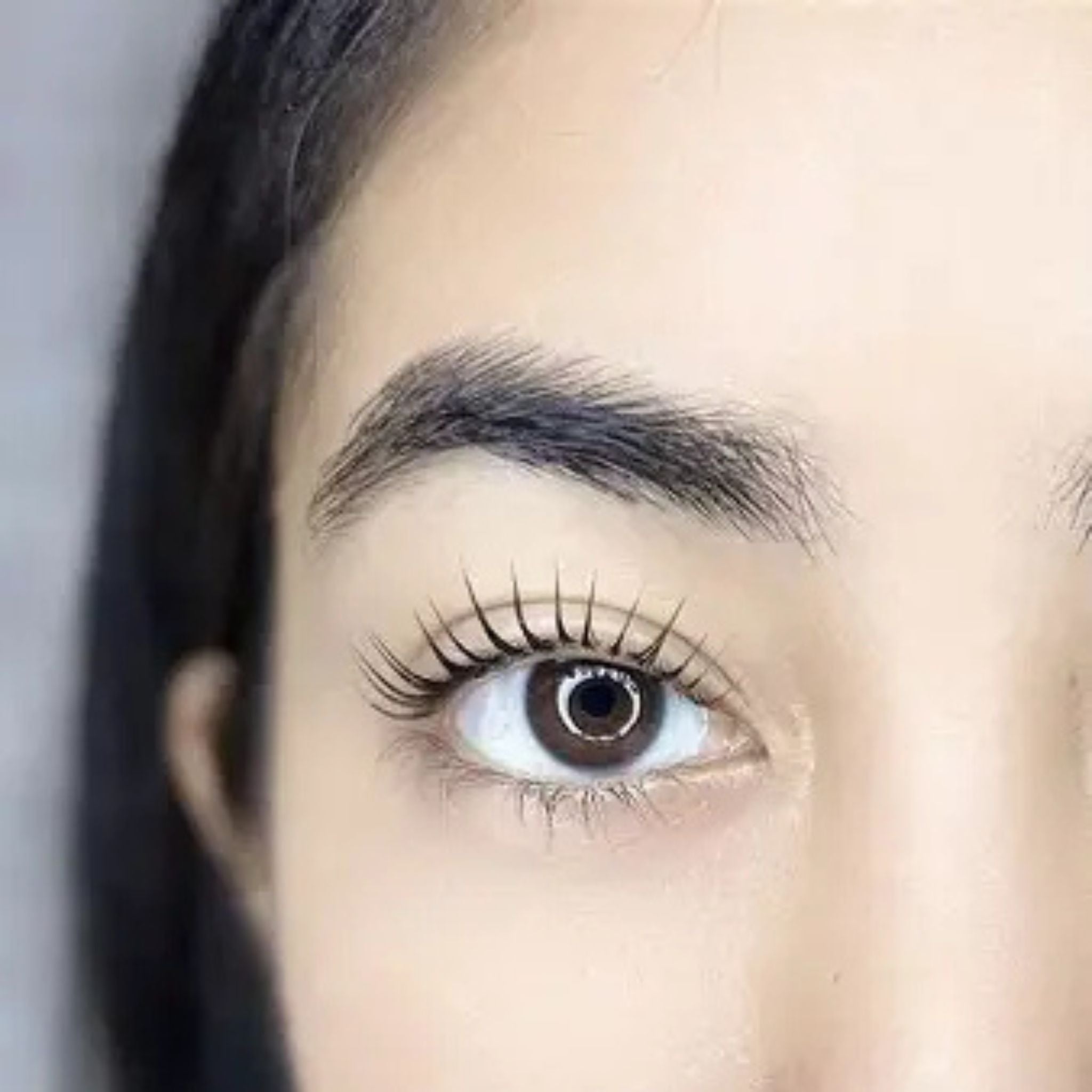 Close-up of a person's eye with long eyelashes against a neutral background