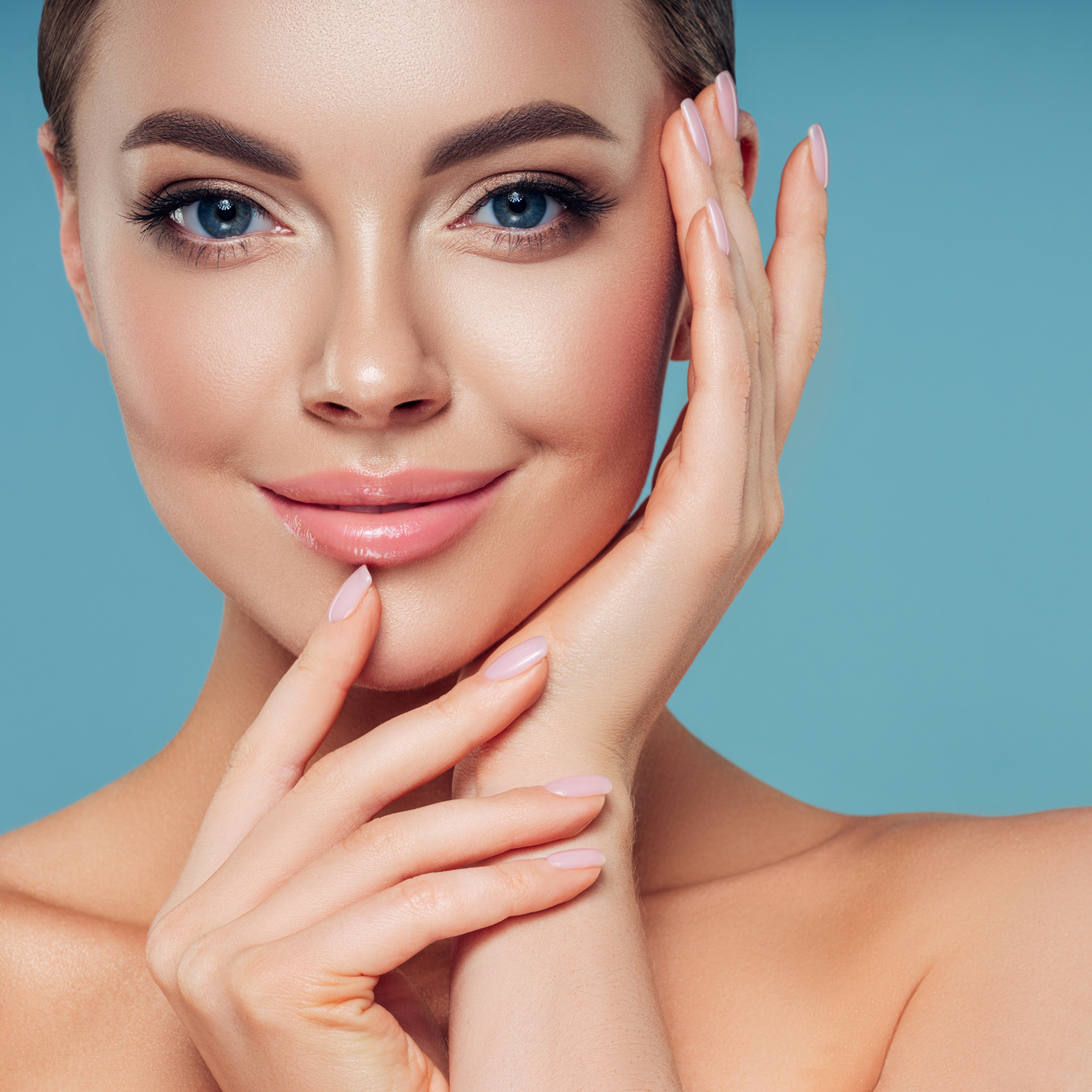 Woman posting cupping her face with her hands with makeup on, with a blue background. 