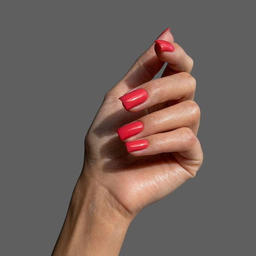 Red nail extensions on model hand with grey background.