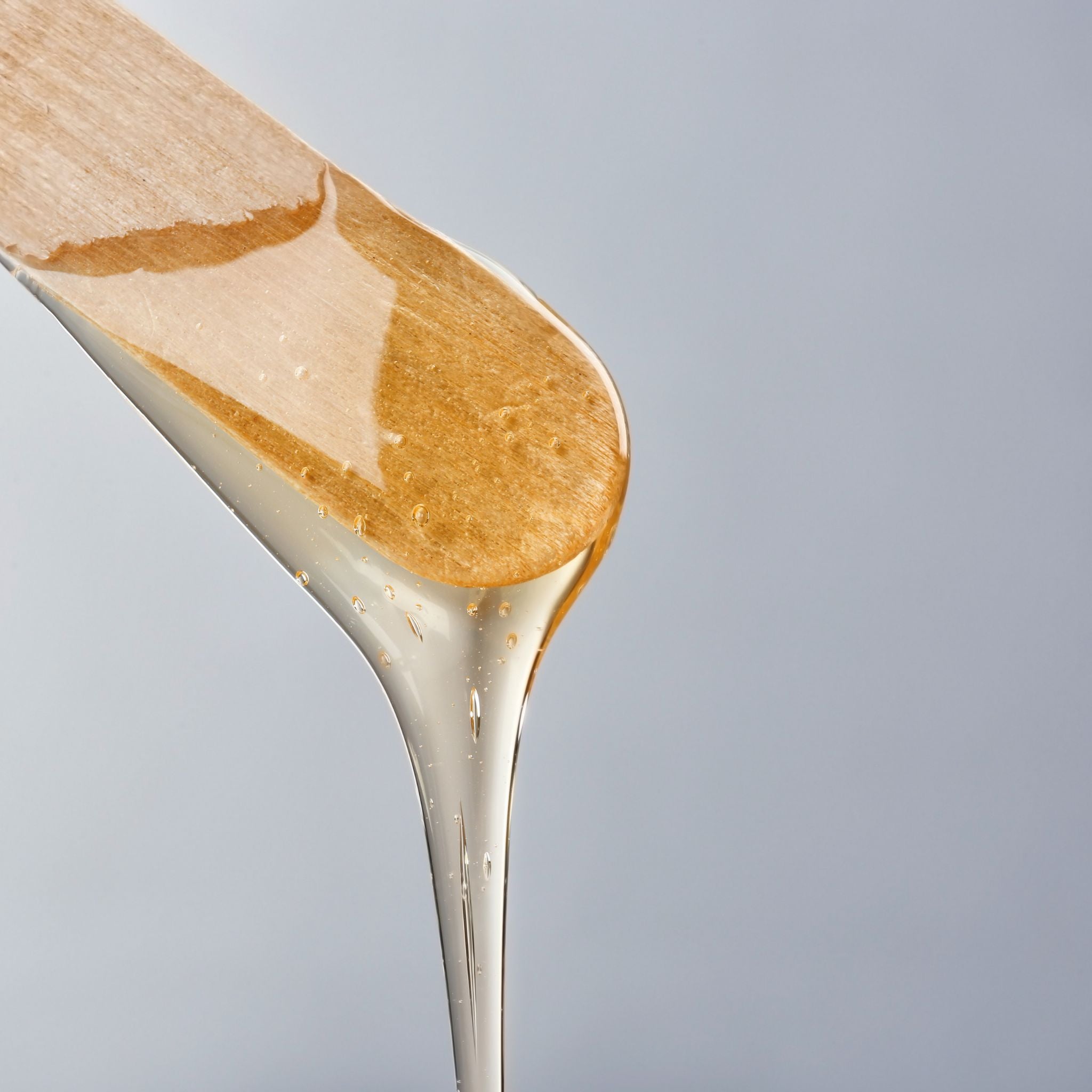 Close-up of a wooden spoon with wax dripping from it against a gray background