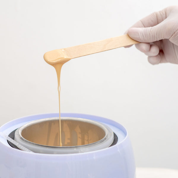 Hand with a wooden spatula dripping wax into a container on a white background