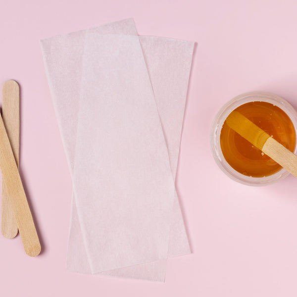 Bowl of wax with a wooden stick, cotton pads, and a pink background